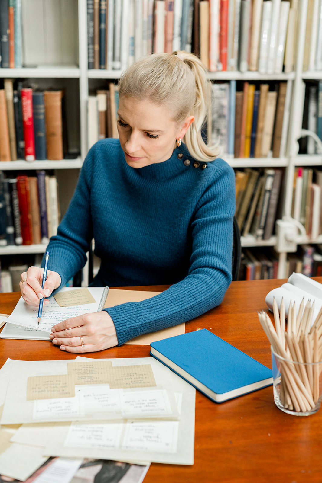 Copywriter, Courtney Fanning leans over a desk and writes in a notebook about her website copywriting services guide.